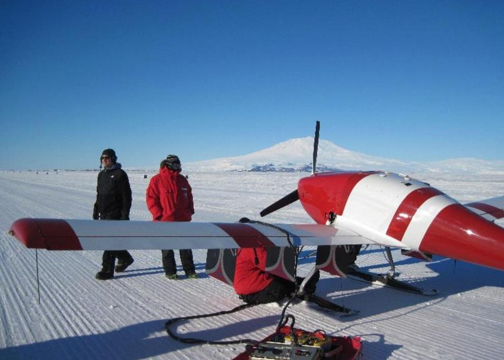 Plane in snow with 2 people working on it.