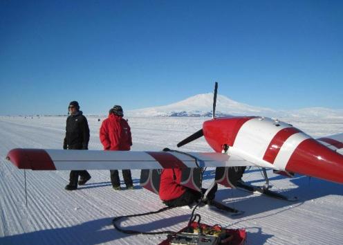 Plane in snow with 2 people working on it.